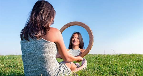 kvinde sidder på græs og kigger glad på sit eget spejlbillede